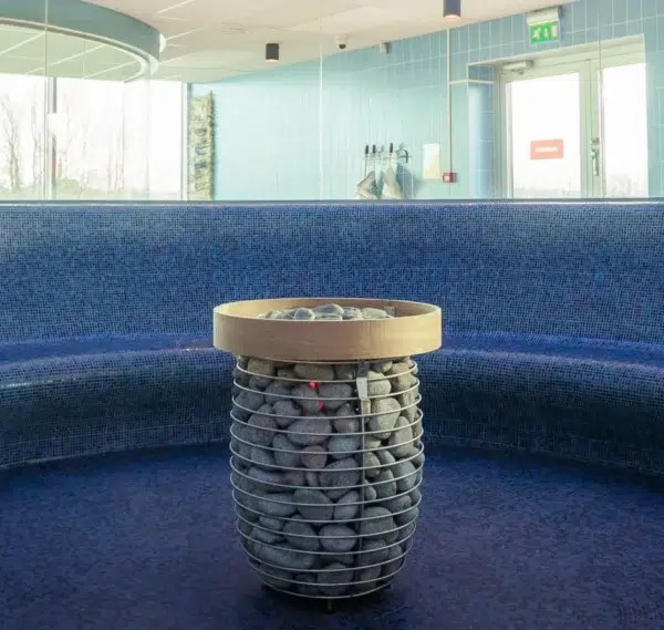 HUUM HIVE electric sauna heater, installed with a wooden safety railing in a curved blue sauna