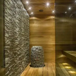 HUUM HIVE Mini electric sauna heater, wide view of sauna installation beside a stone accent wall