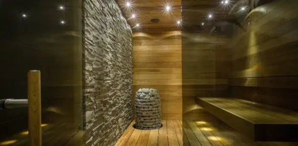 HUUM HIVE Mini electric sauna heater, wide view of sauna installation beside a stone accent wall