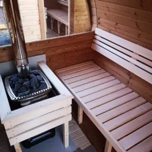 Outdoor barrel sauna, bench and stove behind a wooden guard
