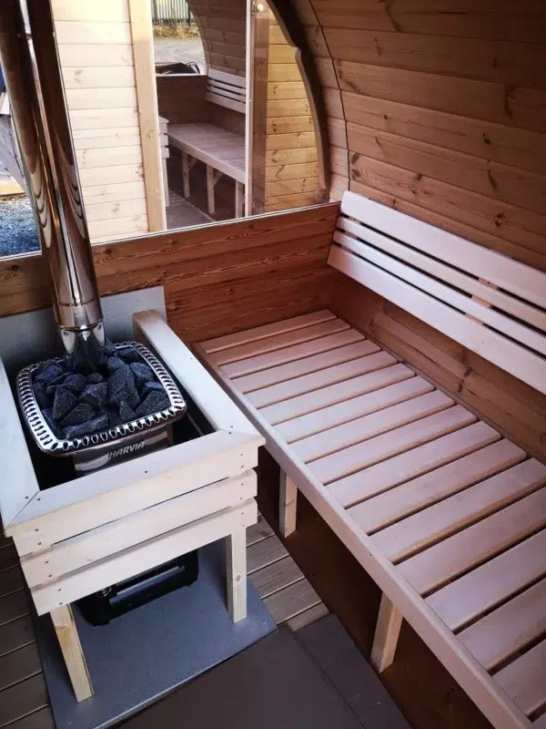 Outdoor barrel sauna, bench and stove behind a wooden guard