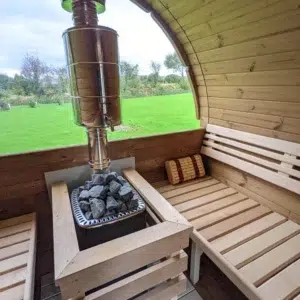 Outdoor barrel sauna, stove and chimney beside a panoramic window