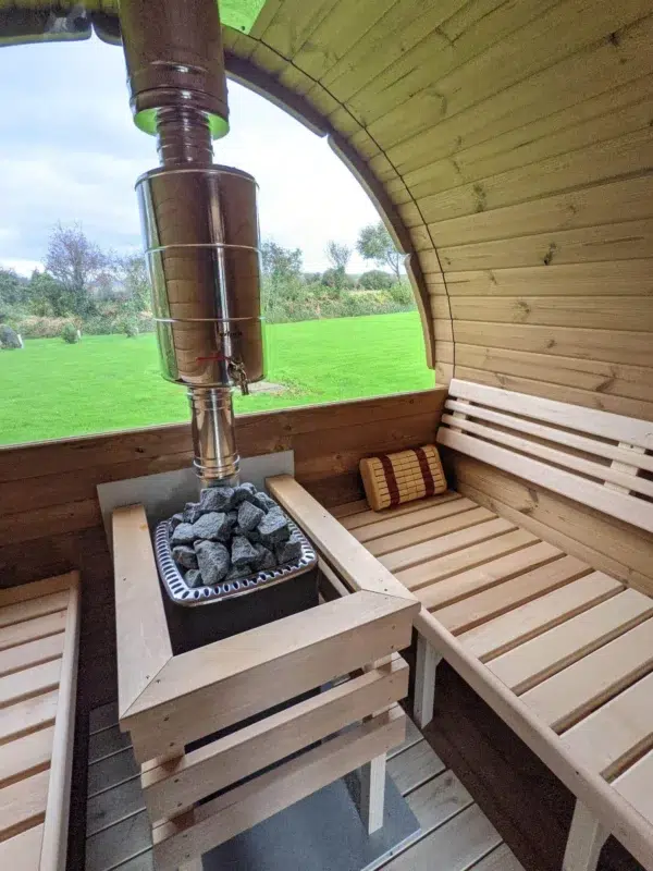 Outdoor barrel sauna, stove and chimney beside a panoramic window