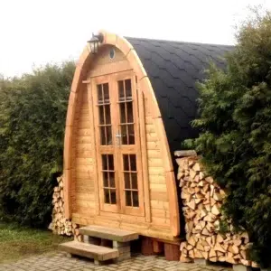 Outdoor pod sauna, front exterior beside stacked firewood