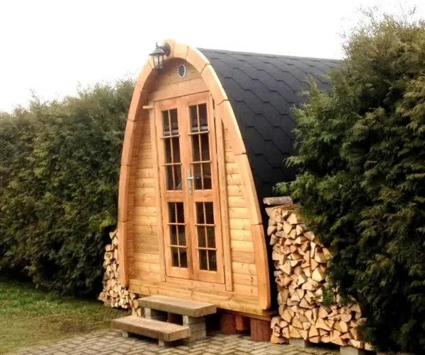 Outdoor pod sauna, front exterior beside stacked firewood
