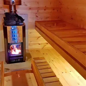Outdoor pod sauna, lit wood-burning stove beside tiered benches