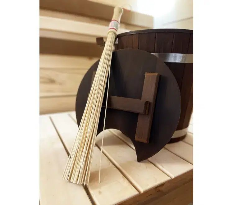 Bamboo sauna whisk beside a wooden bucket on a bench