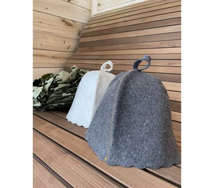 Grey and white felt sauna hats standing on a wooden bench