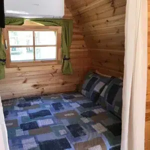 Wooden camping pod, bed beneath a curtained window