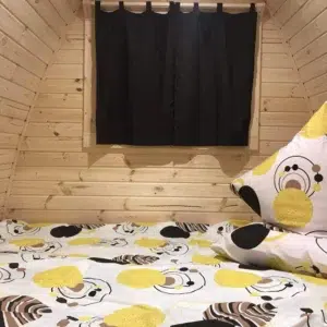 Wooden camping pod, bed beneath a curtained window