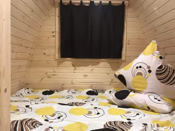 Wooden camping pod, bed beneath a curtained window