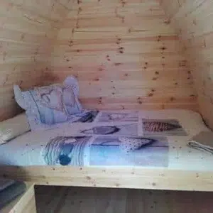 Wooden camping pod, bed beneath a rear window
