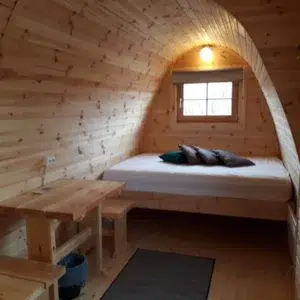 Wooden camping pod, bed beneath a window with side table