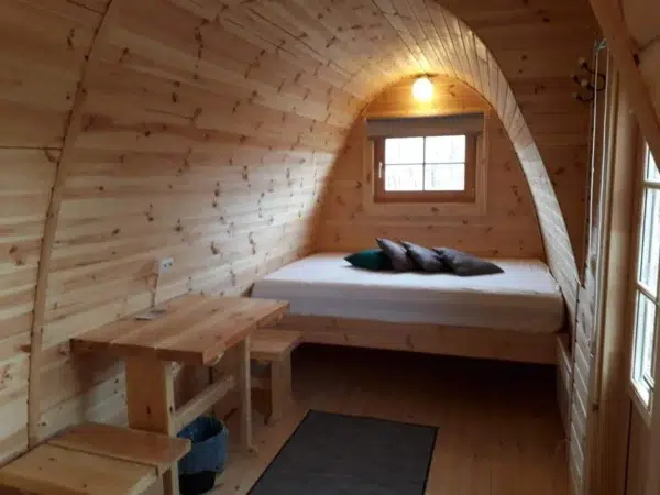 Wooden camping pod, bed beneath a window with side table