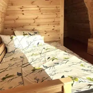 Wooden camping pod, bed beside curved wooden partition