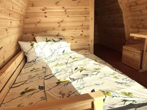 Wooden camping pod, bed beside curved wooden partition