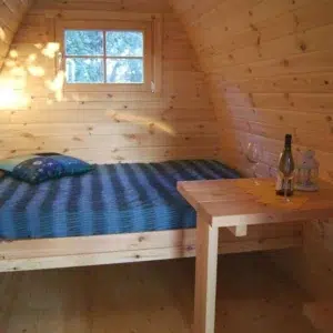 Wooden camping pod, bed with striped bedding and small table