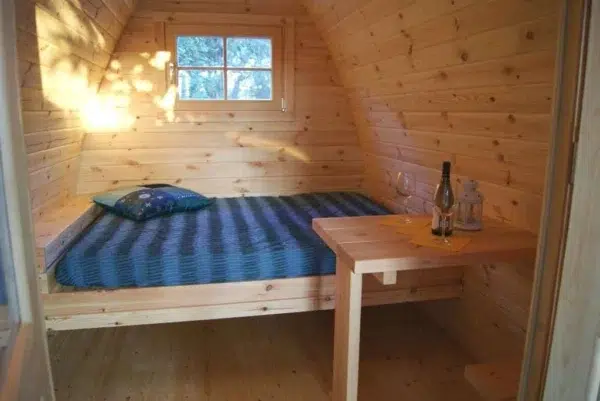 Wooden camping pod, bed with striped bedding and small table