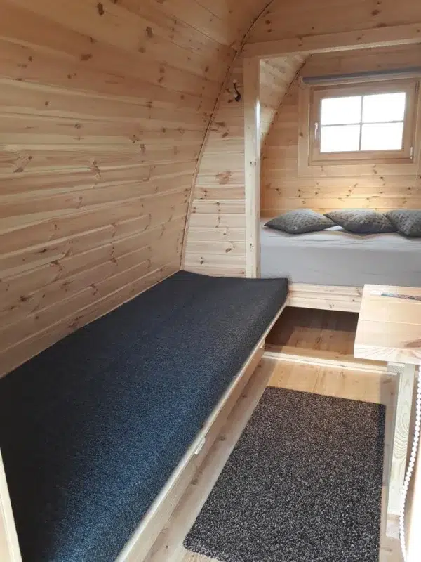 Wooden camping pod, cushioned bench and rear sleeping area