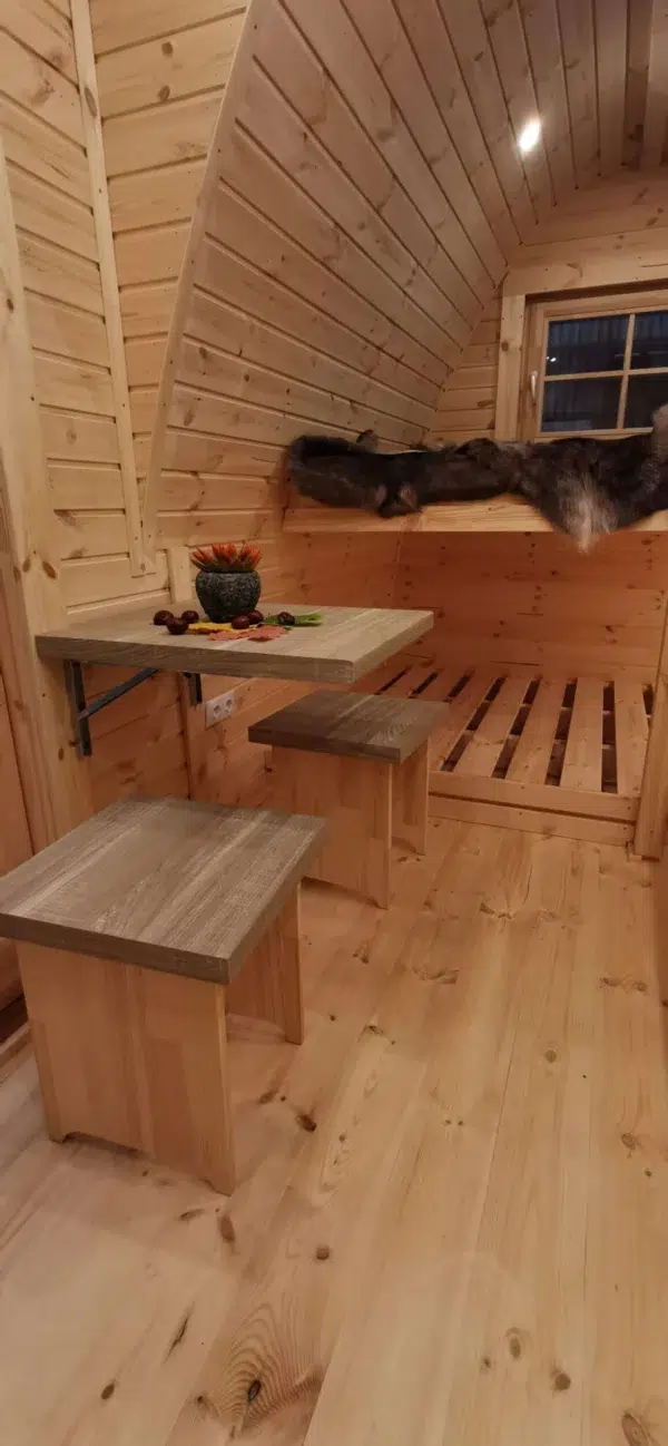 Wooden camping pod, dining table beside raised sleeping platforms