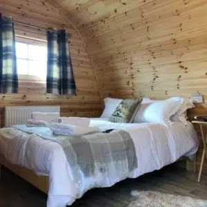 Wooden camping pod, double bed beneath a curtained window