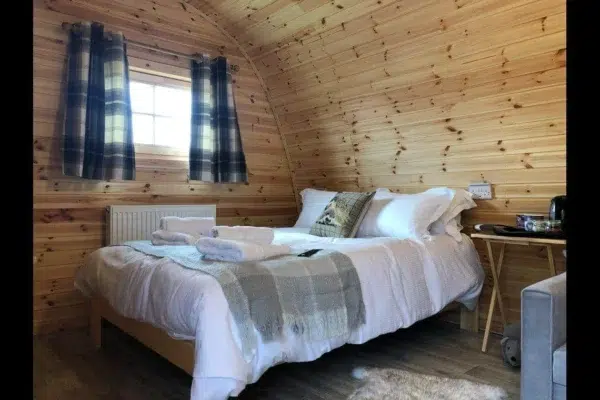 Wooden camping pod, double bed beneath a curtained window