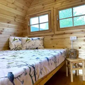 Wooden camping pod, double bed beneath paired windows