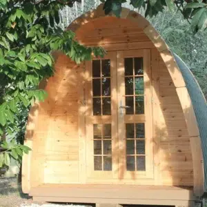 Wooden camping pod, front exterior beneath leafy branches
