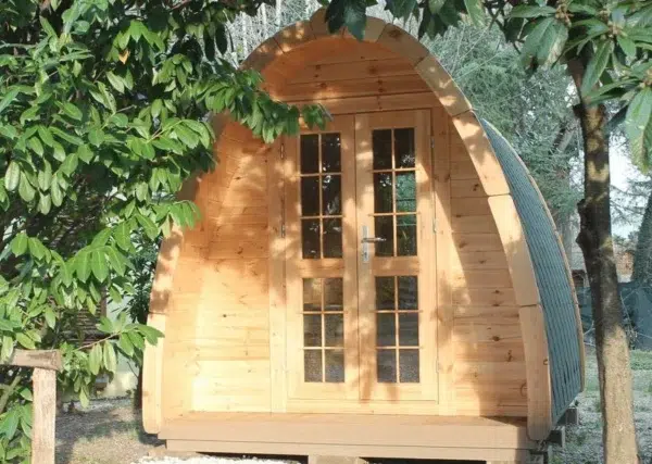 Wooden camping pod, front exterior beneath leafy branches