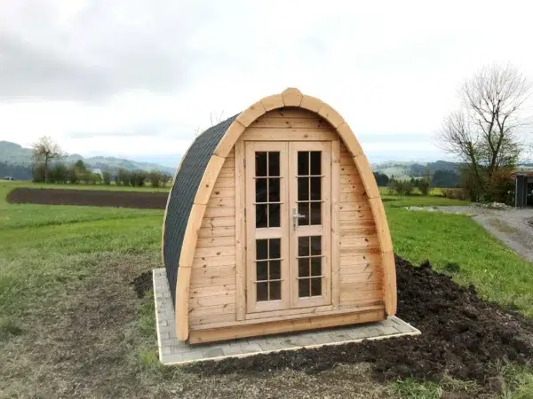 Wooden camping pod, front exterior beside an open field