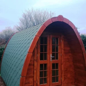Wooden camping pod, front exterior with green shingle roof