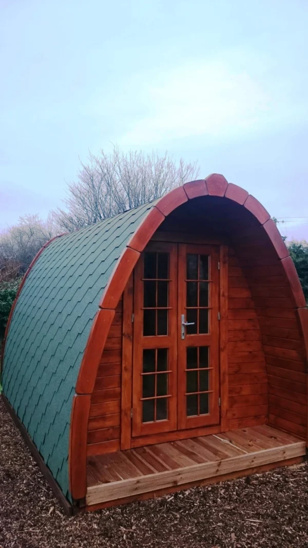 Wooden camping pod, front exterior with green shingle roof
