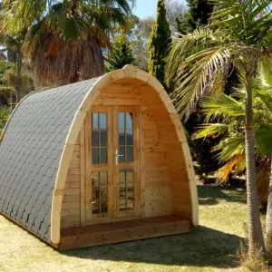 Wooden camping pod, front and side exterior among palm trees