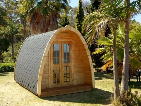 Wooden camping pod, front and side exterior among palm trees