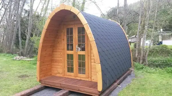 Wooden camping pod, front and side exterior with dark shingle roof