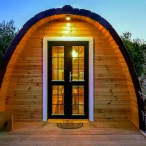 Wooden camping pod, illuminated front entrance at dusk