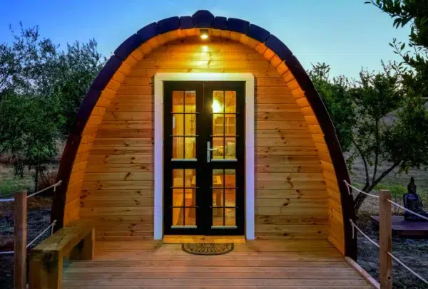Wooden camping pod, illuminated front entrance at dusk