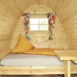 Wooden camping pod, interior bed beneath a curtained window