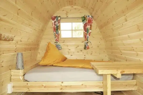 Wooden camping pod, interior bed beneath a curtained window