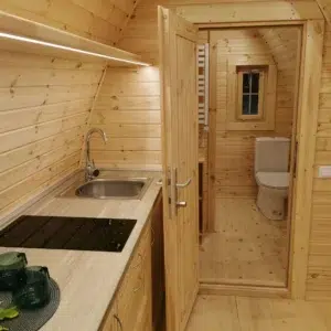 Wooden camping pod, kitchenette beside open bathroom doorway