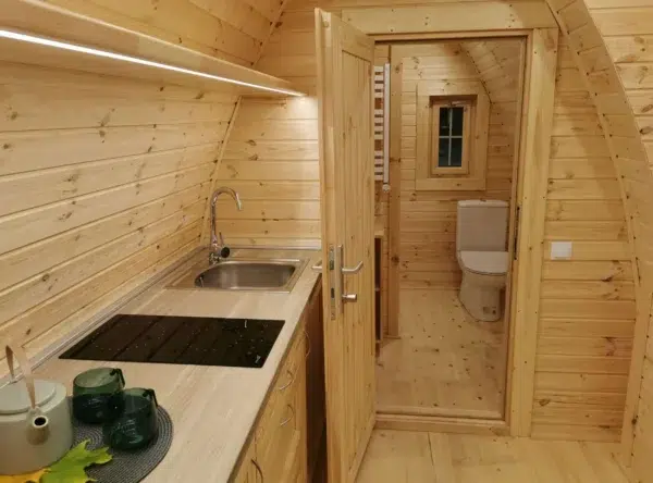 Wooden camping pod, kitchenette beside open bathroom doorway