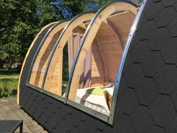 Wooden camping pod, large curved roof glazing viewed from outside