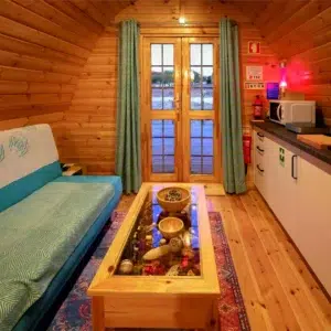 Wooden camping pod, living area with sofa, table and kitchenette