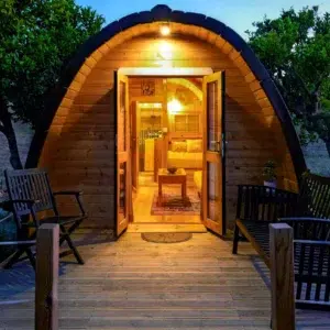 Wooden camping pod, open illuminated entrance at dusk