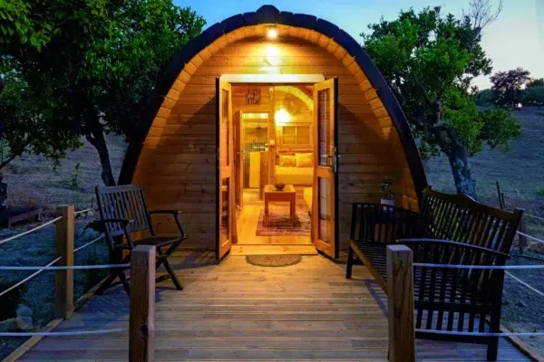 Wooden camping pod, open illuminated entrance at dusk