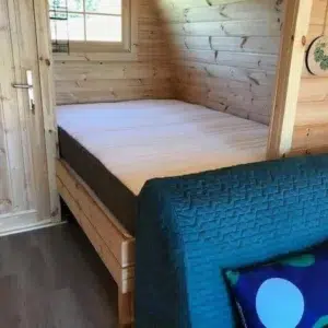 Wooden camping pod, separate bed behind cushioned seating