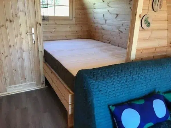 Wooden camping pod, separate bed behind cushioned seating