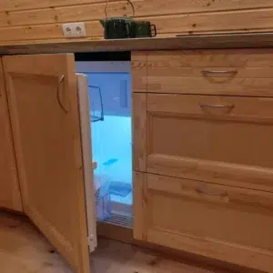 Wooden camping pod, under-counter refrigerator behind open cabinet door