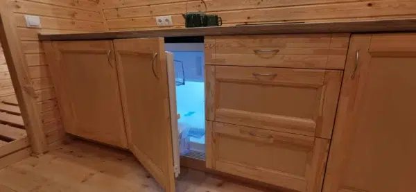 Wooden camping pod, under-counter refrigerator behind open cabinet door