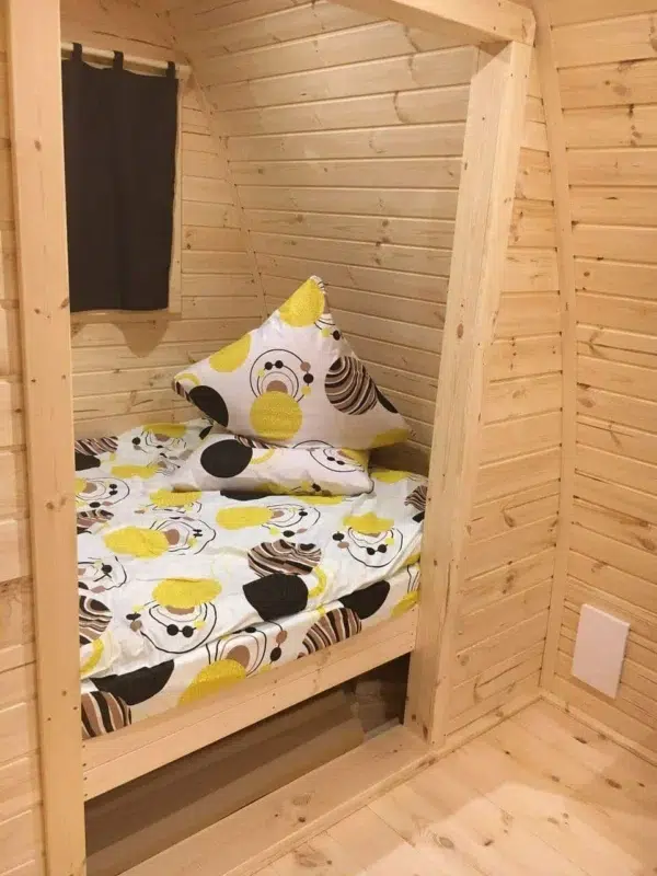 Wooden camping pod, view through doorway to a made-up bed